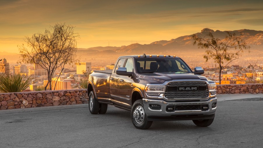 A dark 2020 Ram 3500 Heavy Duty Limited Crew Cab Dually pickup truck with a cityscape, mountains, and sunset in the background