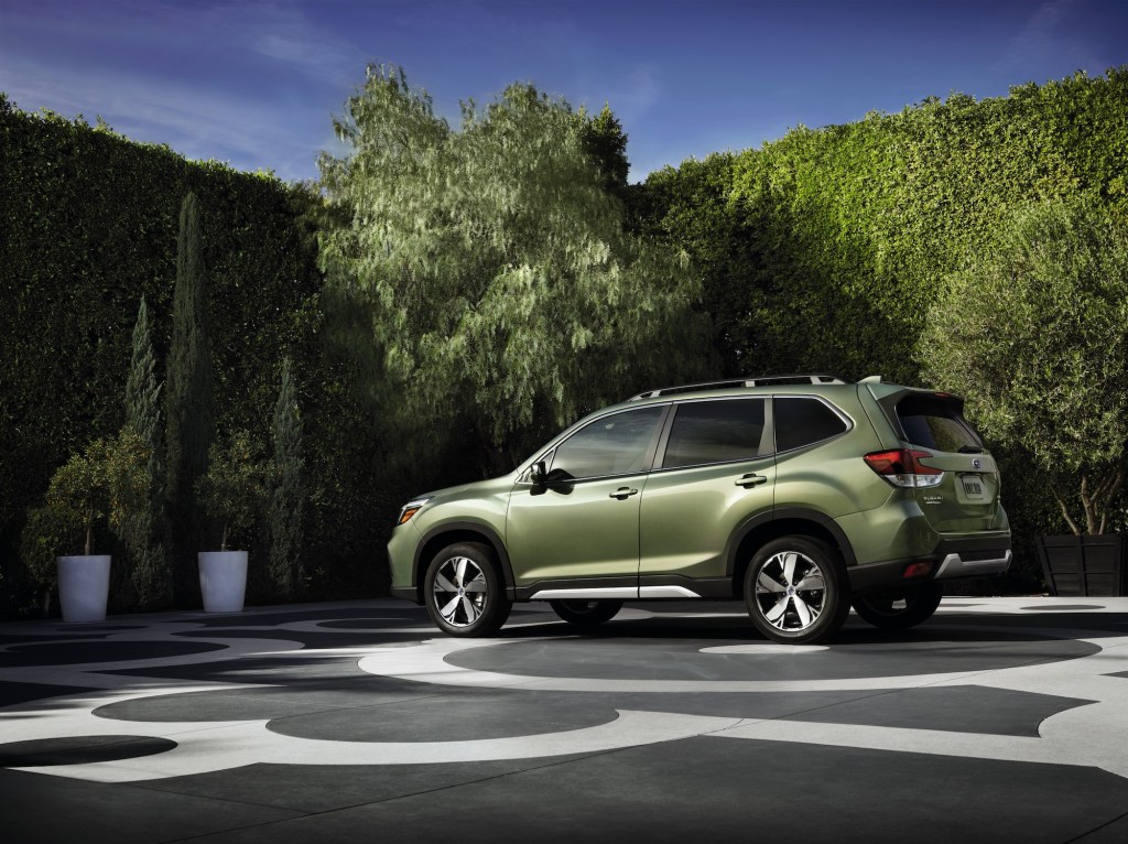 A green 2020 Subaru Forester parked on a patterned concrete slab surrounded by potted trees and shrubbery