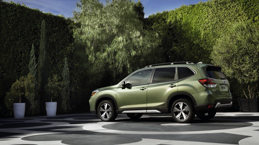A green 2020 Subaru Forester parked on a patterned concrete slab surrounded by potted trees and shrubbery