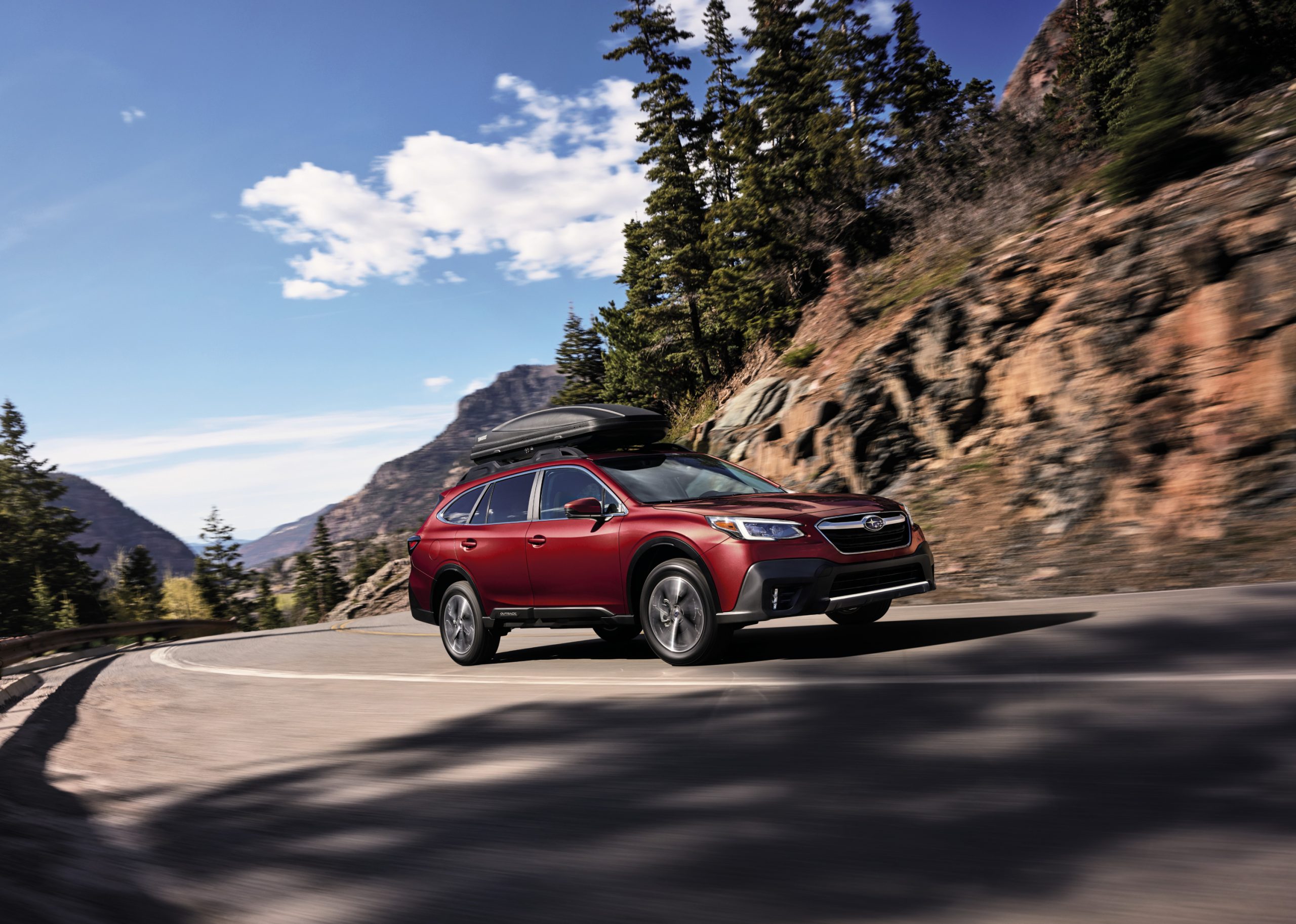 A red 2020 Subaru Outback driving down a highway road