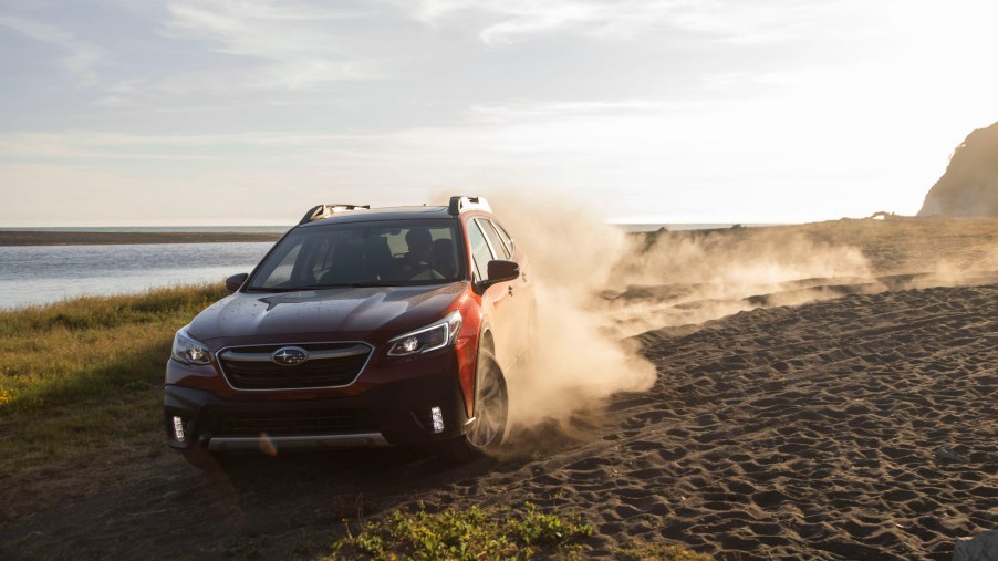 A red 2020 Subaru Outback kicks up sand as it drives on a beach