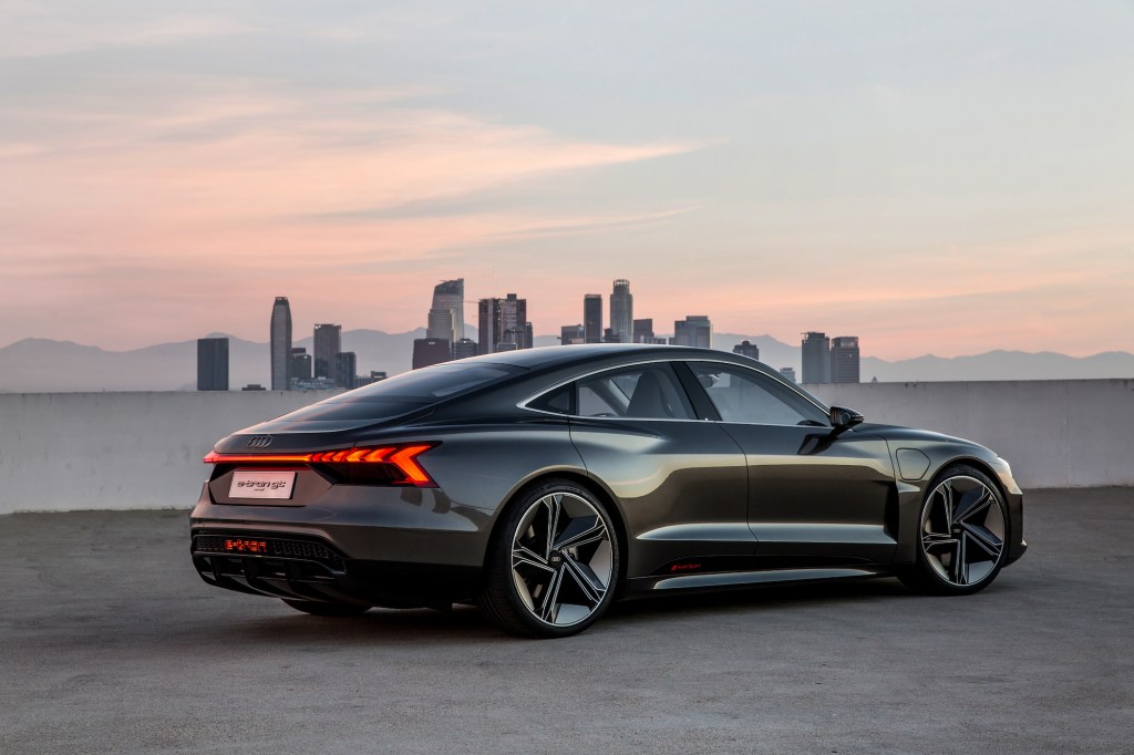 A dark-colored 2021 Audi e-tron GT concept in front of a cityscape and mountain range