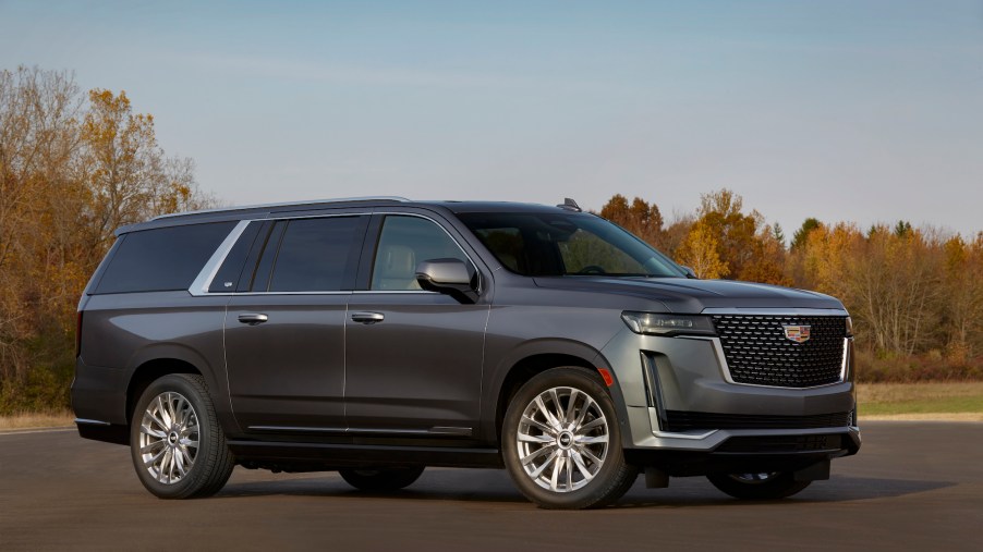 A dark-gray metallic 2021 Cadillac Escalade turbodiesel SUV parked on asphalt surrounded by trees with autumn leaves