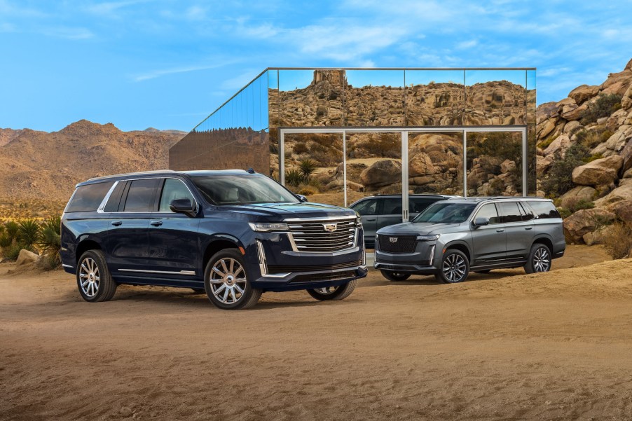 Two 2021 Cadillac Escalade ESV full-size SUVs parked in front of a small mirrored building in a mountainous desert