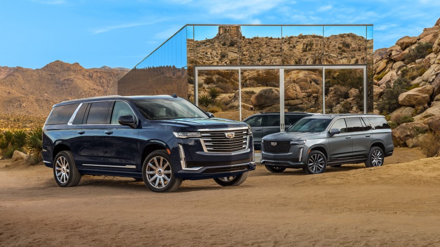 Two 2021 Cadillac Escalade ESV full-size SUVs parked in front of a small mirrored building in a mountainous desert