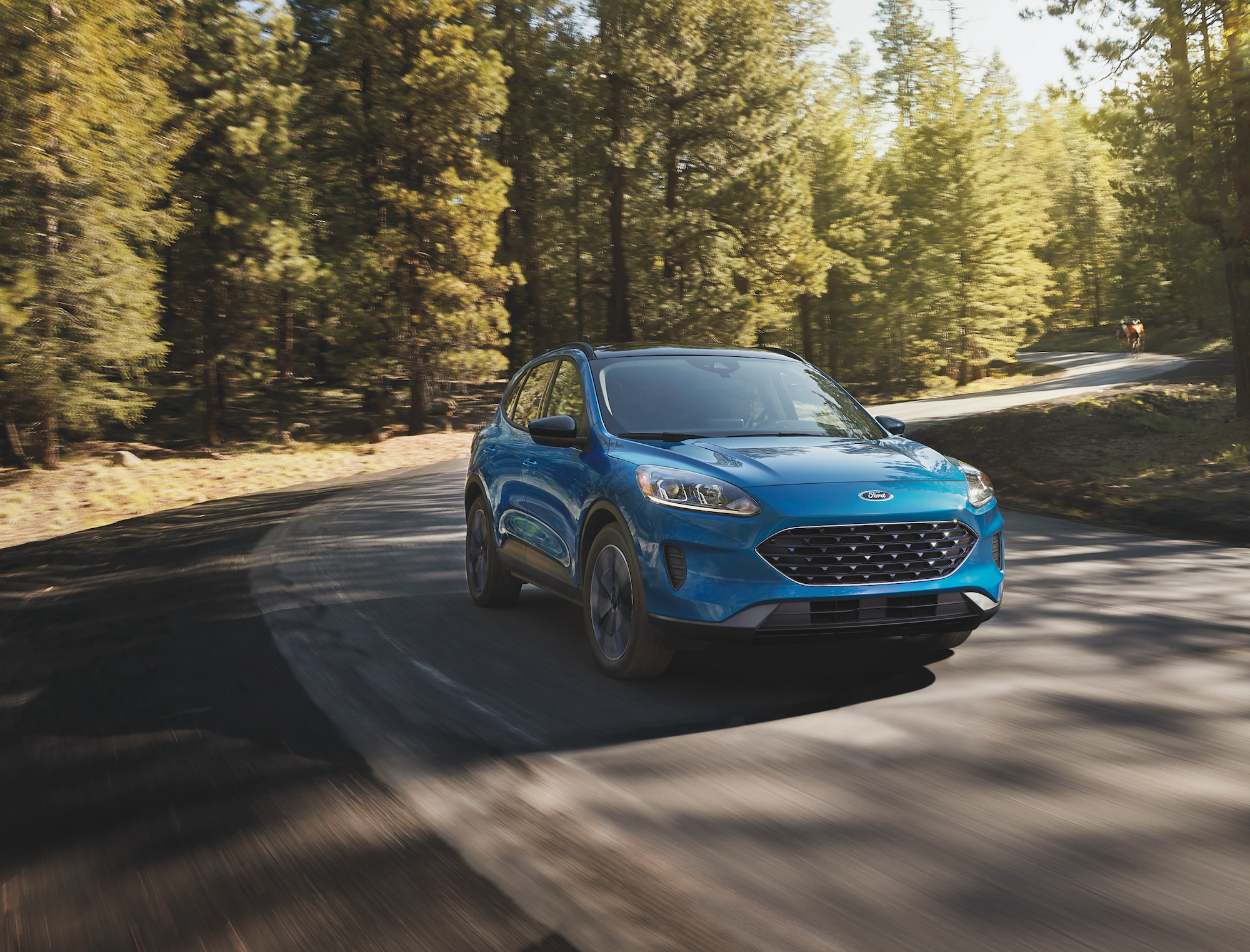 A blue 2021 Ford Escape compact SUV travels on a winding road through pine trees