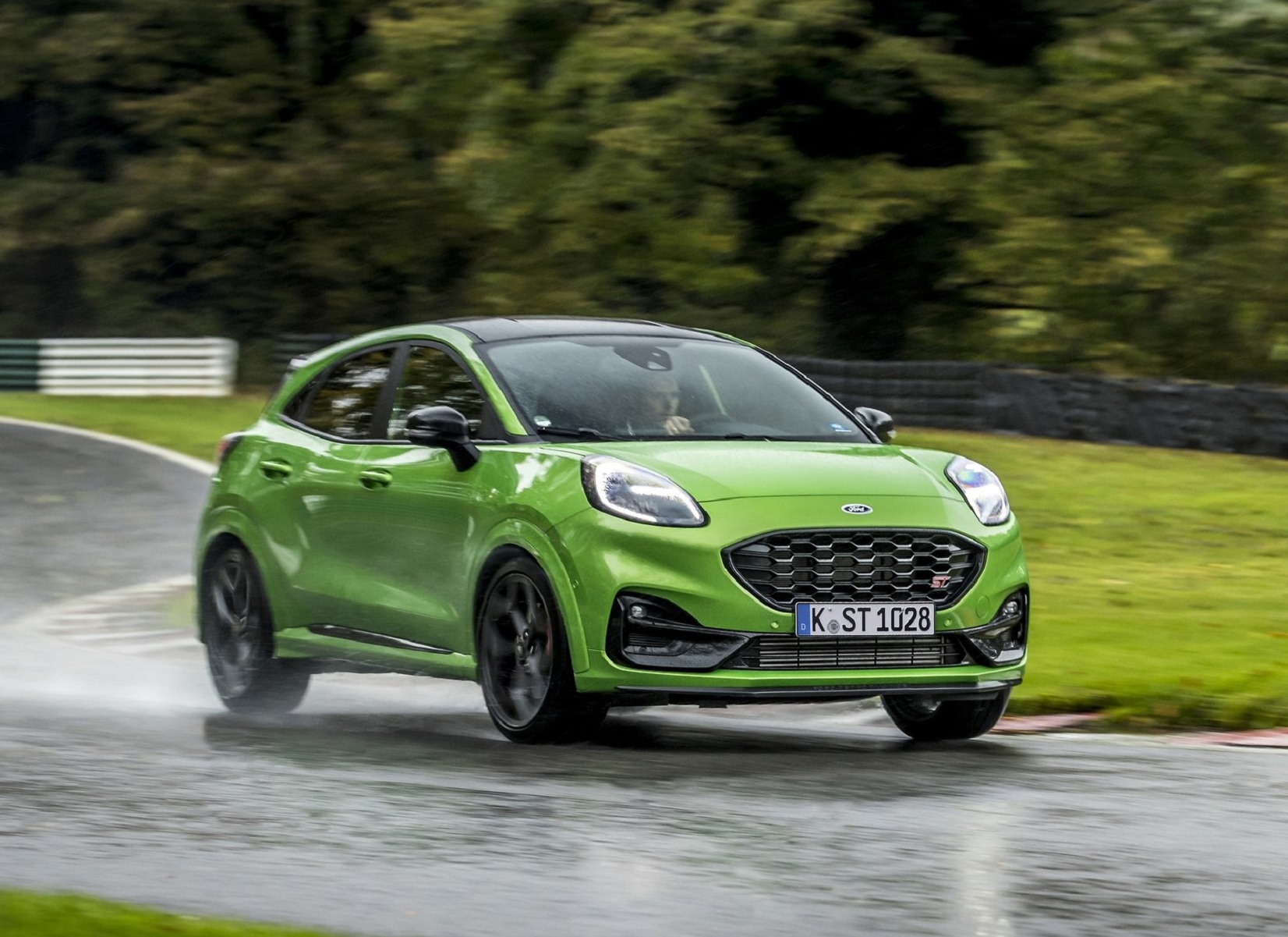 A green 2021 Ford Puma ST drives around a wet racetrack in the forest