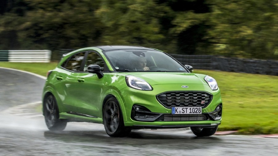 A green 2021 Ford Puma ST drives around a wet racetrack in the forest