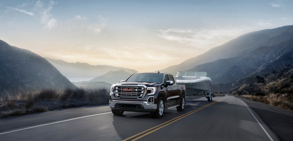 A black 2021 GMC Sierra SLT four-door pickup truck towing a boat on a two-lane highway in the mountains