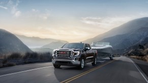 A black 2021 GMC Sierra SLT four-door pickup truck towing a boat on a two-lane highway in the mountains