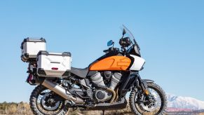 An orange 2021 Harley-Davidson Pan America 1250 Special in the desert equipped with accessory luggage cases