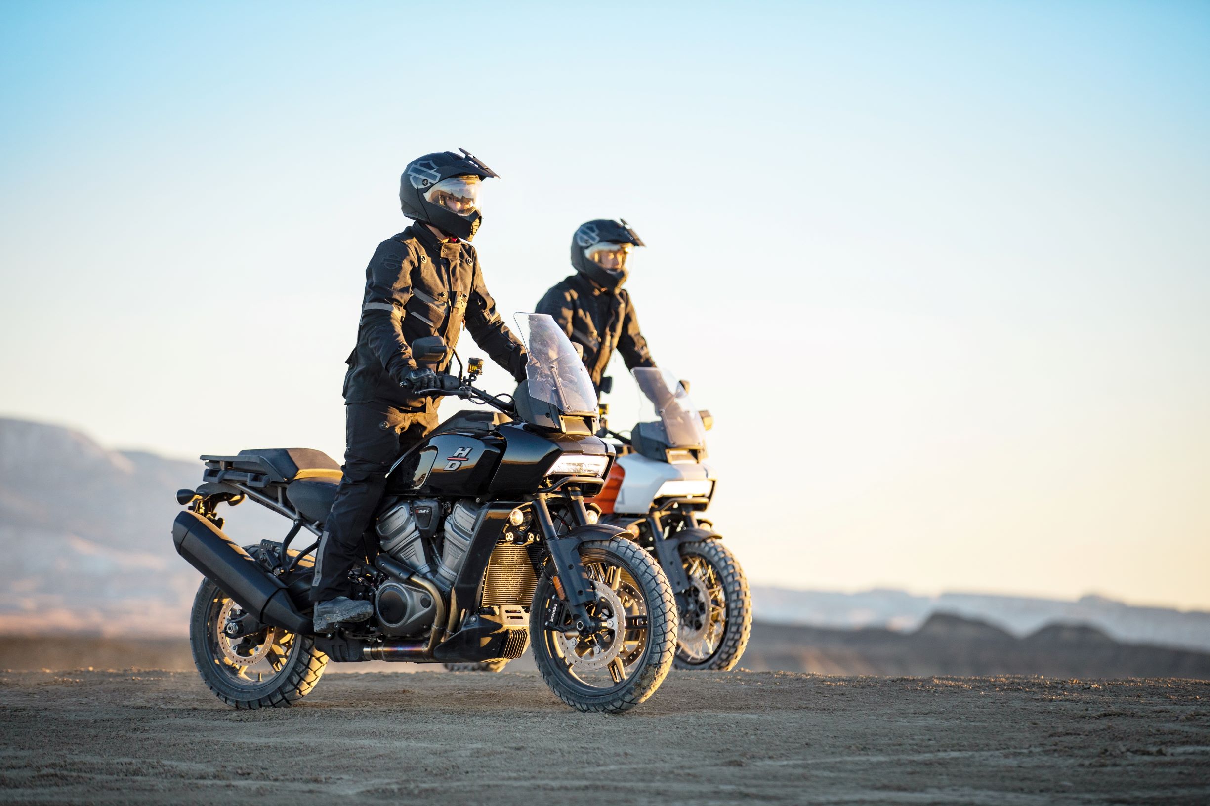 A rider on a black 2021 Harley-Davidson Pan America 1250 in front of an orange 1250 Special in the desert