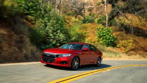 A red 2021 Honda Accord Hybrid travels on a two-lane highway on a hillside