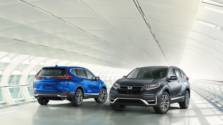 Two 2021 Honda CR-V Touring models, one blue and one dark gray, parked next to each other on a white covered bridge