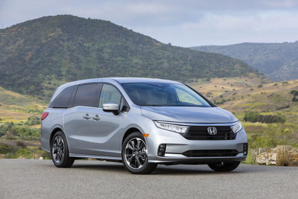 A silver 2021 Honda Odyssey minivan parked in front of grassy hills