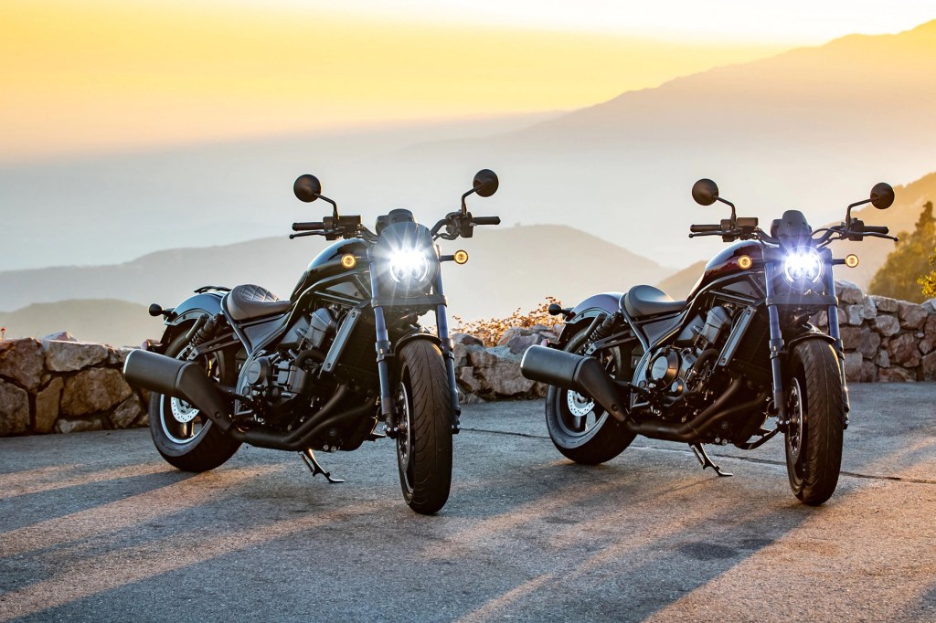 An accessorized black and maroon 2021 Honda Rebel 1100 parked on a mountainside road at sunset