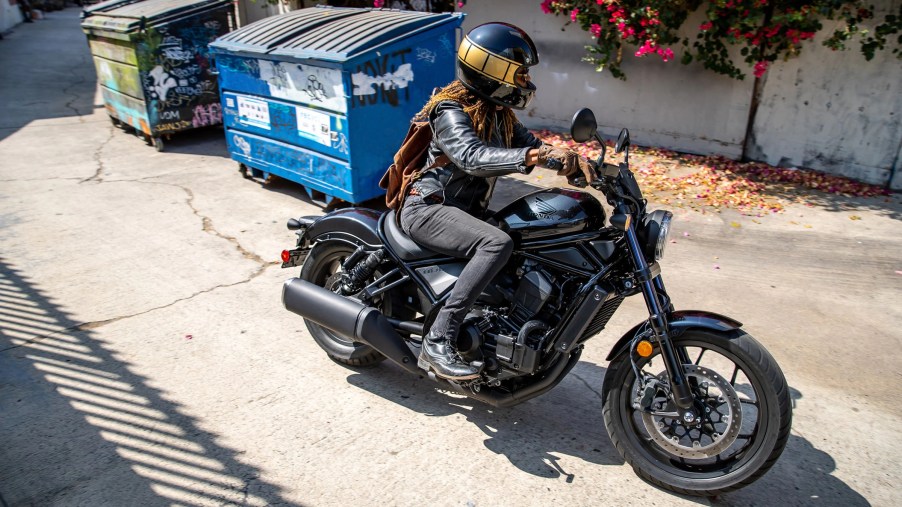 A rider takes a black 2021 Honda Rebel 1100 through an alley