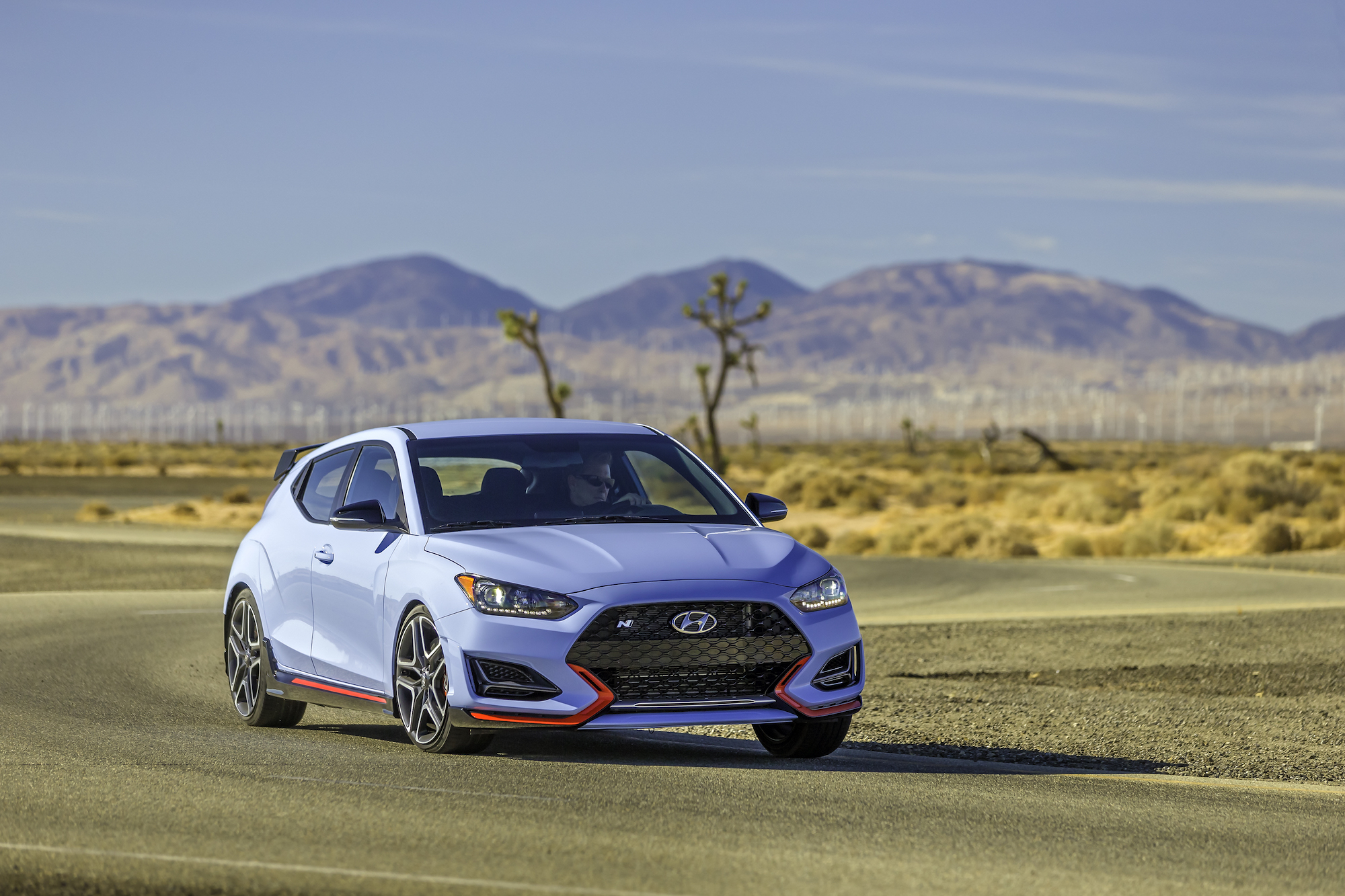 A sky-blue 2021 Hyundai Veloster N sports car travels on a winding road course in a desert