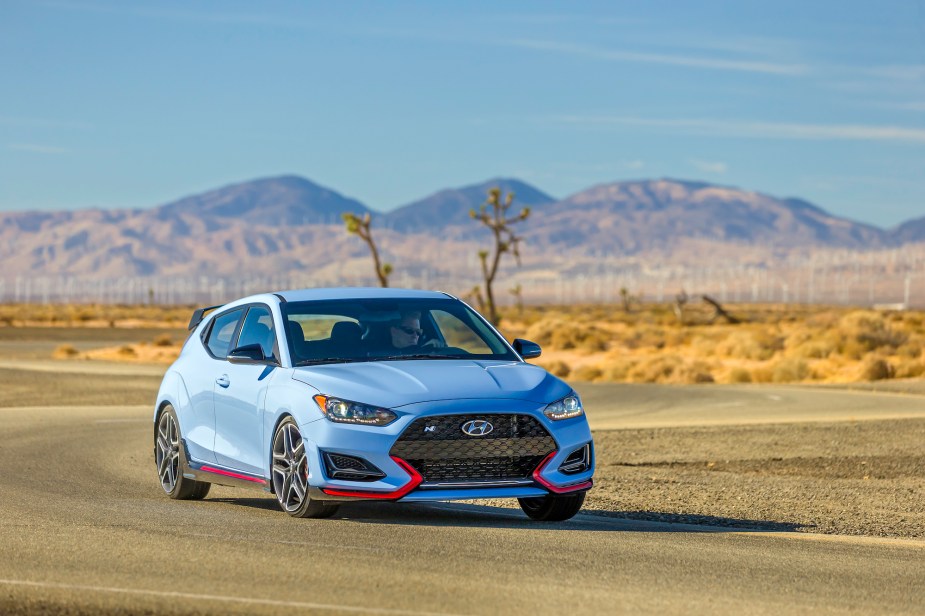 A sky-blue 2021 Hyundai Veloster N sports car travels on a winding road course in a desert