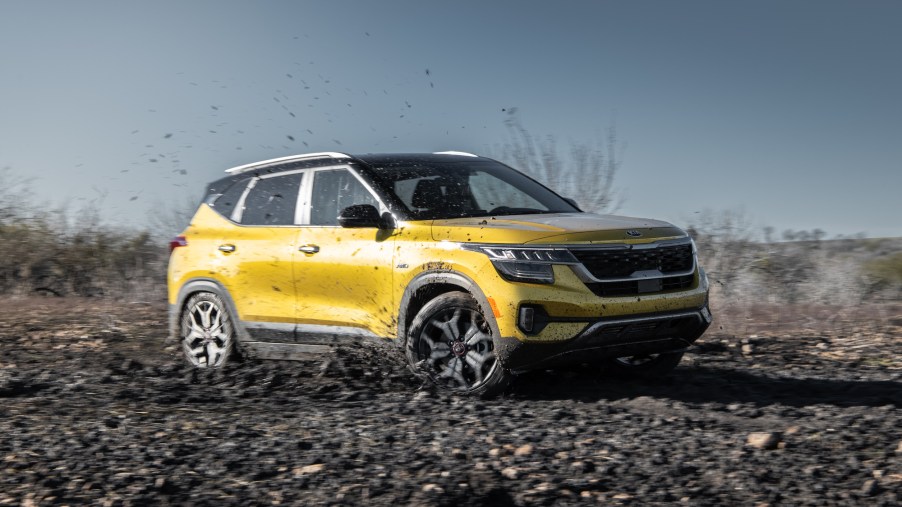 A yellow 2021 Kia Seltos all-wheel-drive compact SUV drives through the mud on a sunny day