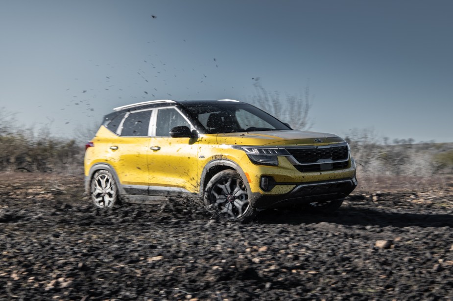 A yellow 2021 Kia Seltos all-wheel-drive compact SUV drives through the mud on a sunny day