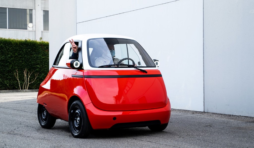 A red-and-white 2021 Microlino 2.0 pre-production prototype with two passengers