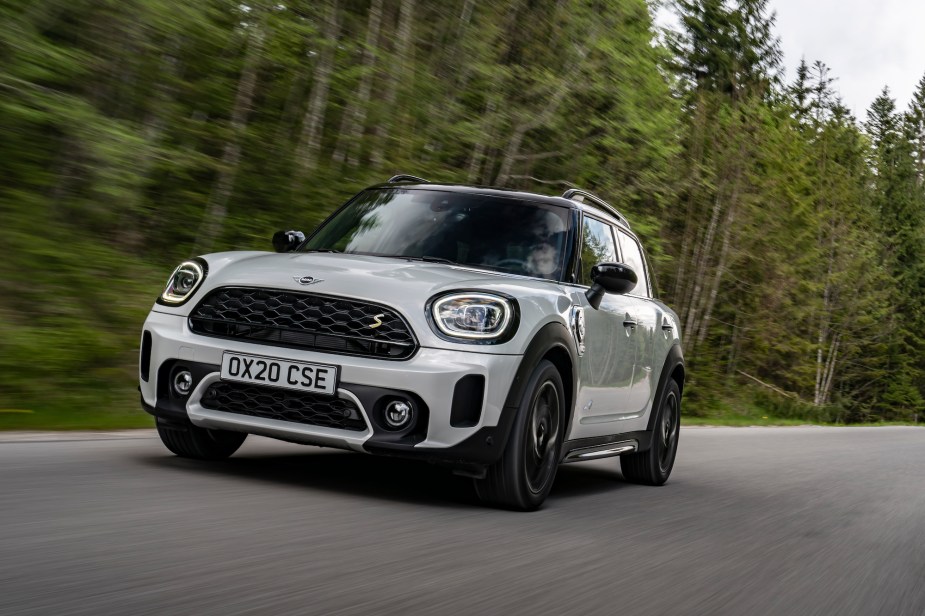 A white 2021 Mini Cooper Countryman travels on a road lined by pine trees on a cloudy day