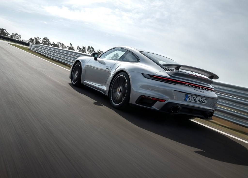 The rear 3/4 view of a silver 2021 Porsche 911 Turbo S driving around a racetrack corner
