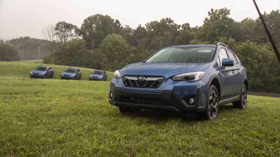 A blue 2021 Subaru Crosstrek Limited parked in the grass for a photoshoot with 3 other Subarus in the far-off distance