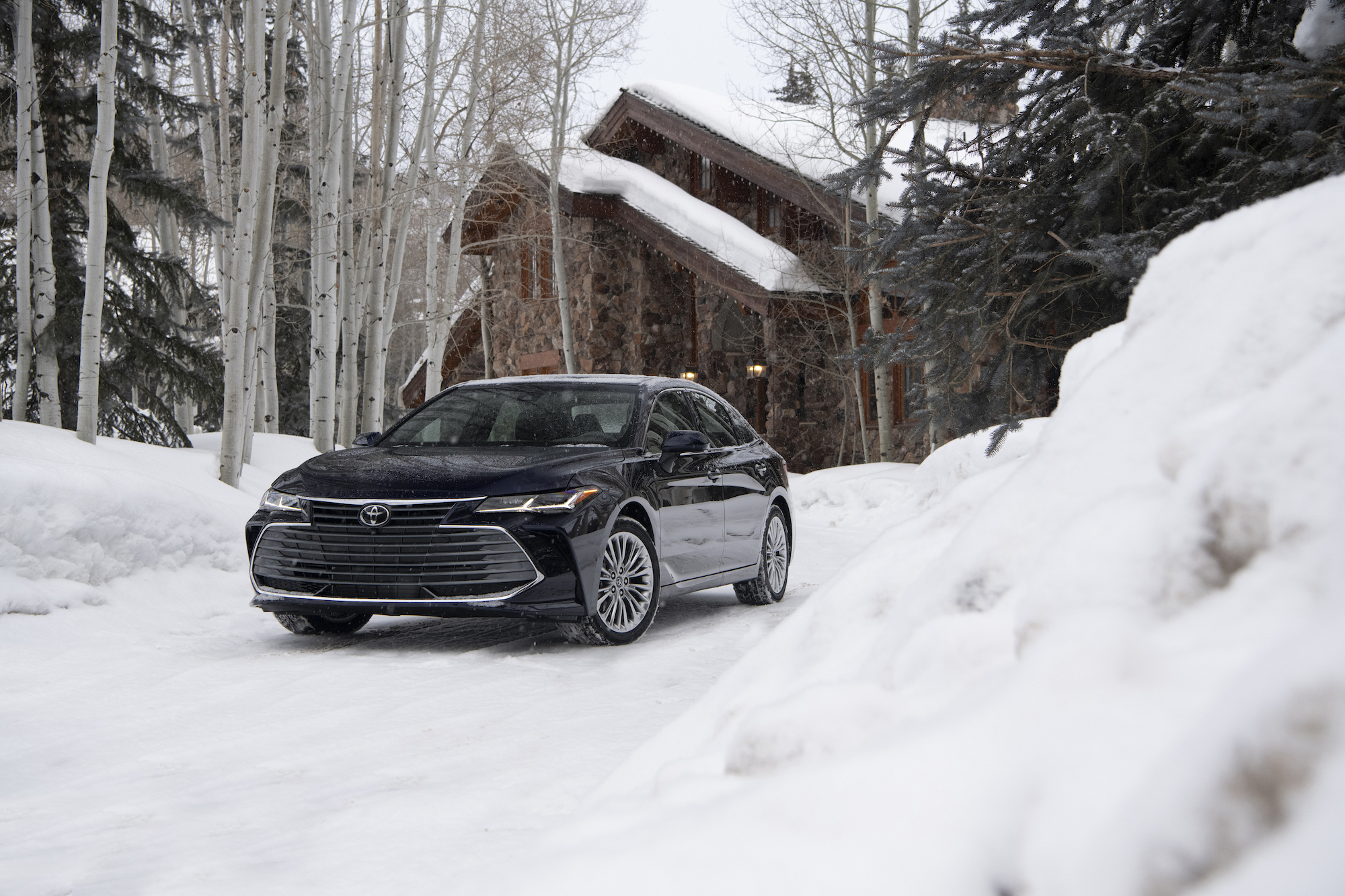 A dark-blue 2021 Toyota Avalon Limited AWD parked in the snow outside a modern cabin in the woods