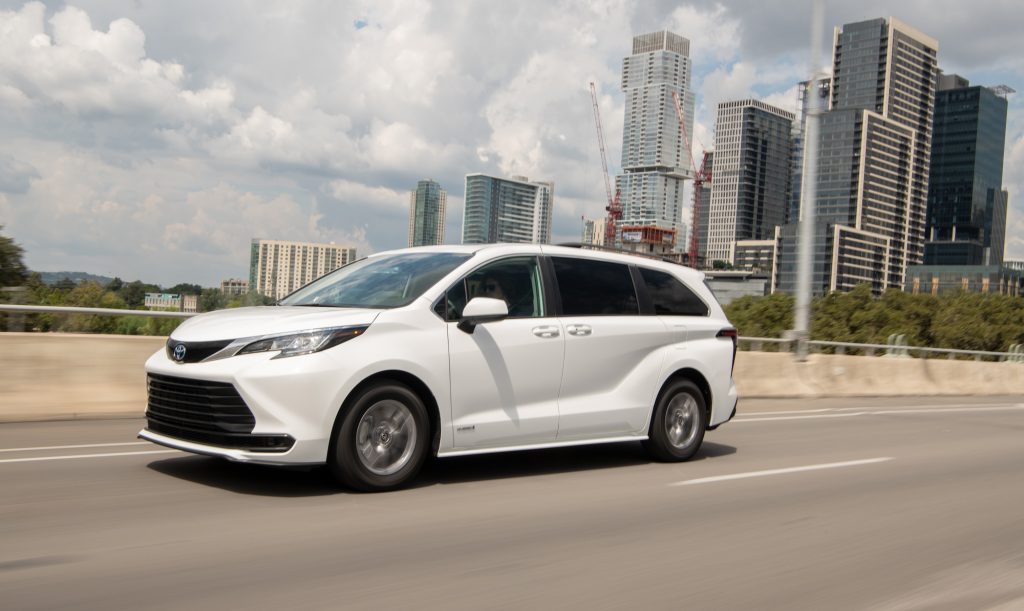 A white 2021 Toyota Sienna LE hybrid minivan travels on a bridge in a city