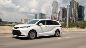 A white 2021 Toyota Sienna LE hybrid minivan travels on a bridge in a city