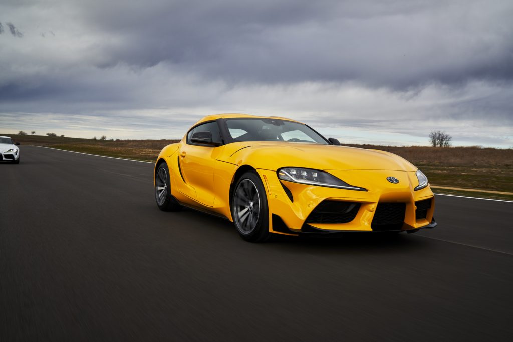 A yellow 2021 Toyota Supra sports car driving on a race track with a cloudy sky in the background