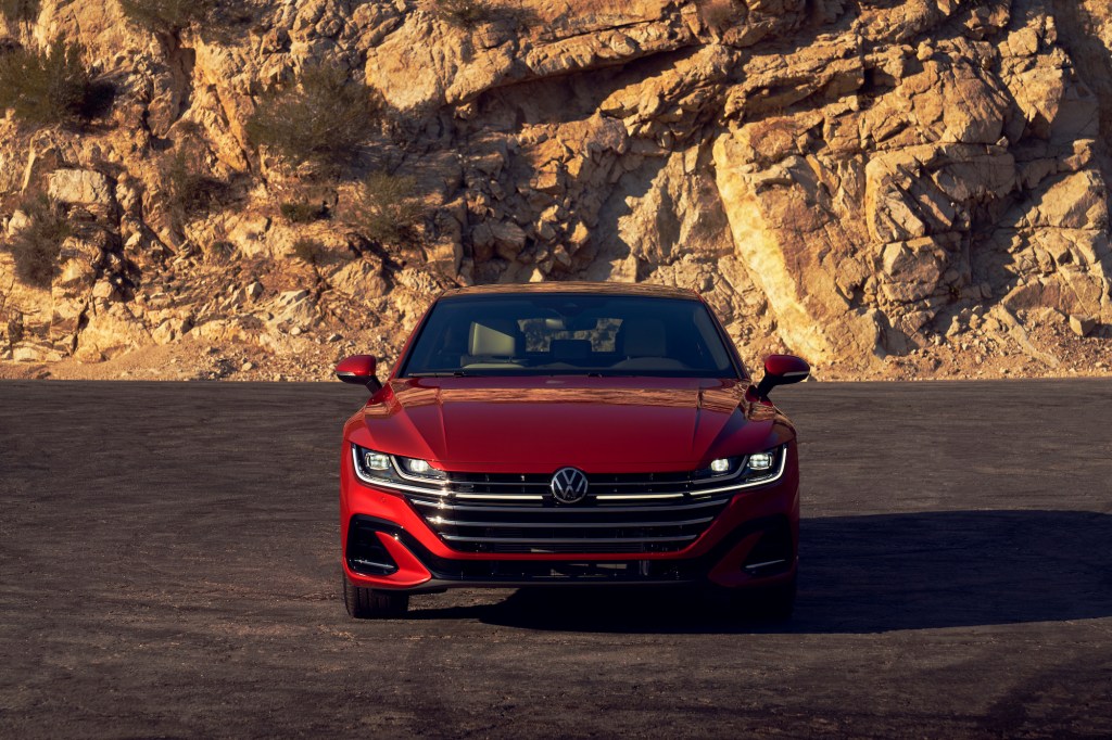Front view of a red 2021 Volkswagen Arteon with its lights on, parked on a slab of asphalt in front of a rocky mountain