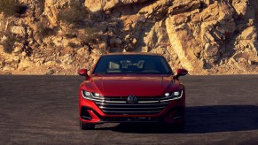 Front view of a red 2021 Volkswagen Arteon with its lights on, parked on a slab of asphalt in front of a rocky mountain