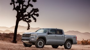 A light gray 2022 Nissan Frontier sits beside a tree among a rugged dessert