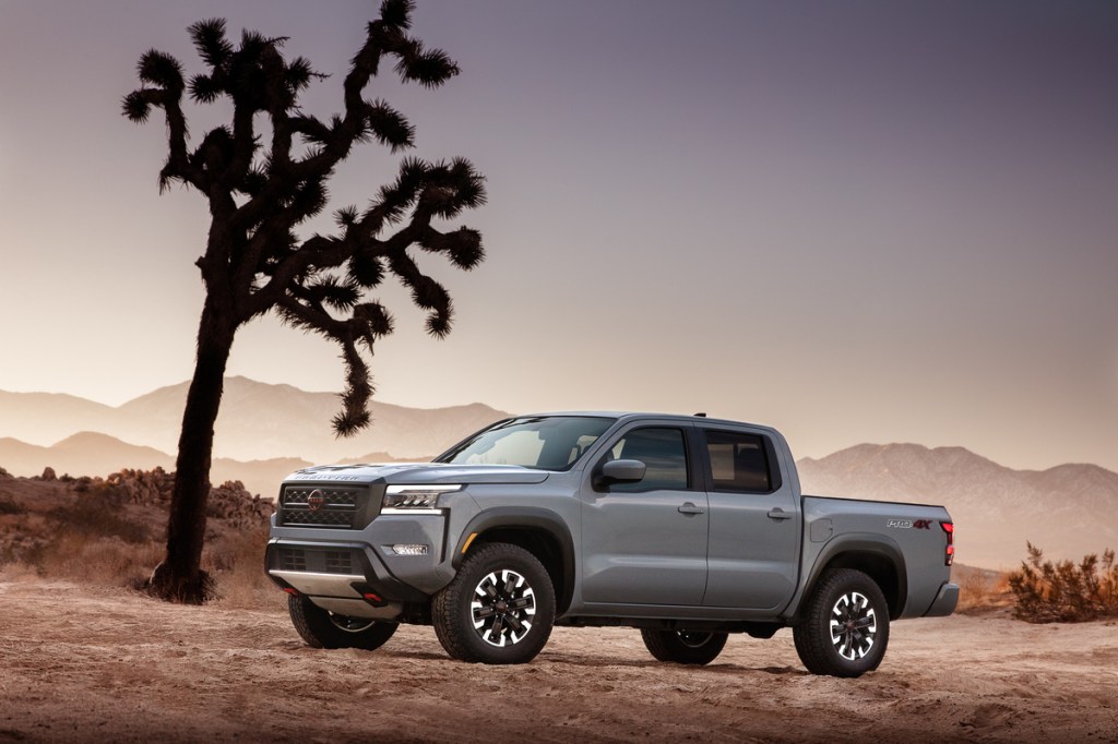 A light gray 2022 Nissan Frontier, a midsize truck, sits beside a tree among a rugged dessert