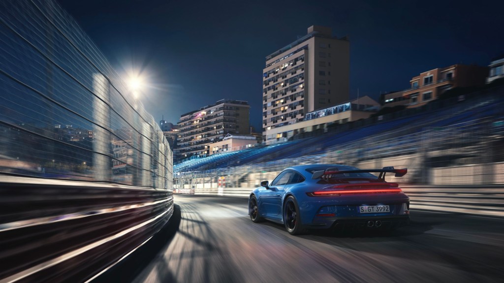 The rear 3/4 view of a blue 2022 Porsche 911 GT3 on a racetrack at night