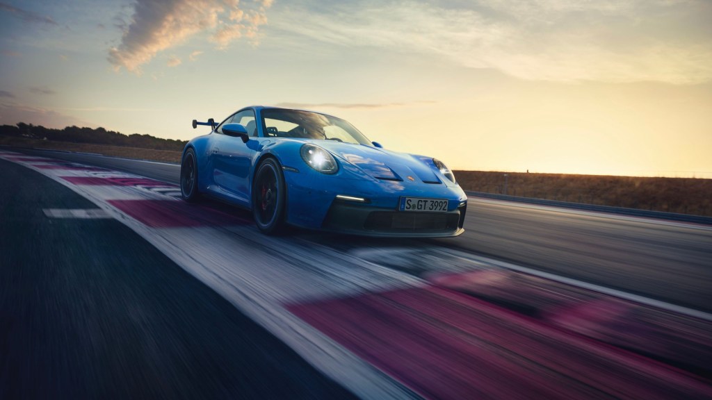 A blue 2022 Porsche 911 GT3 drives around a racetrack at sunset