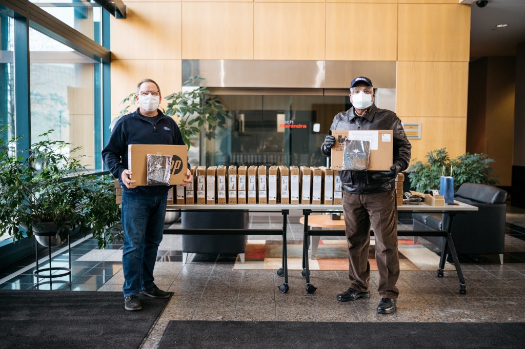 Two men stand holding laptops to be donated to the Girls in Engineering Academy