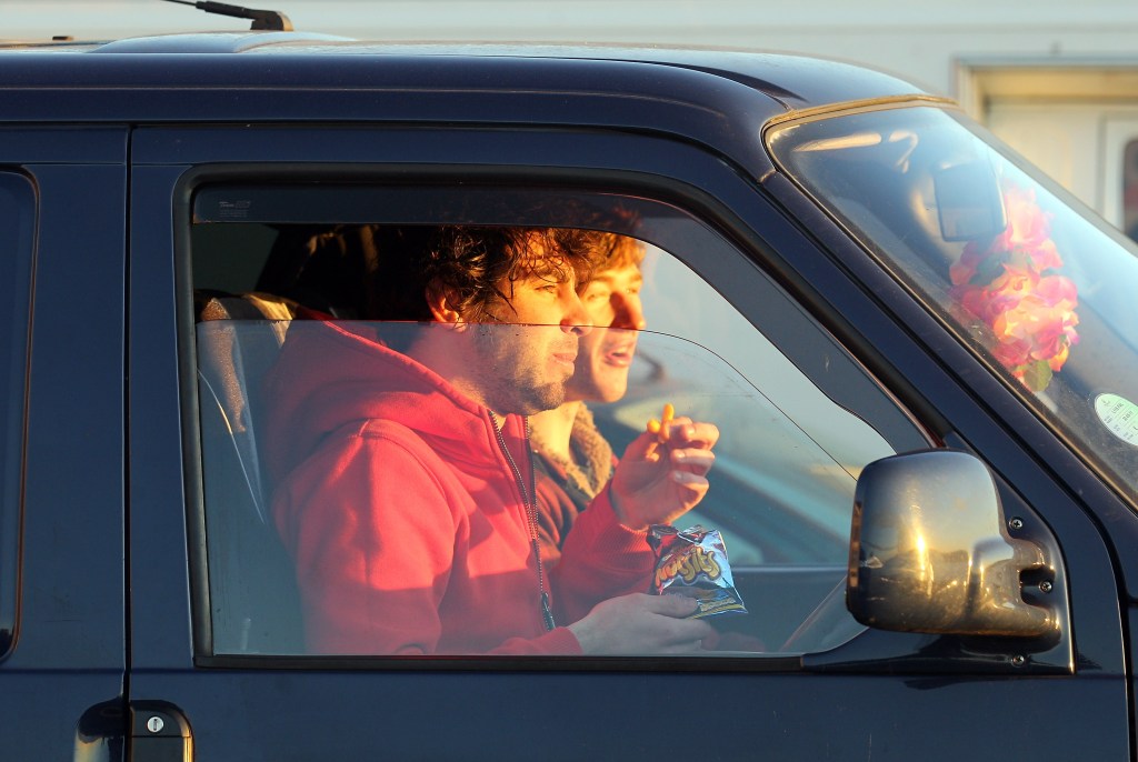 Surfers watch and eat snacks from their parked cars above the beach the Cornish winter waves.