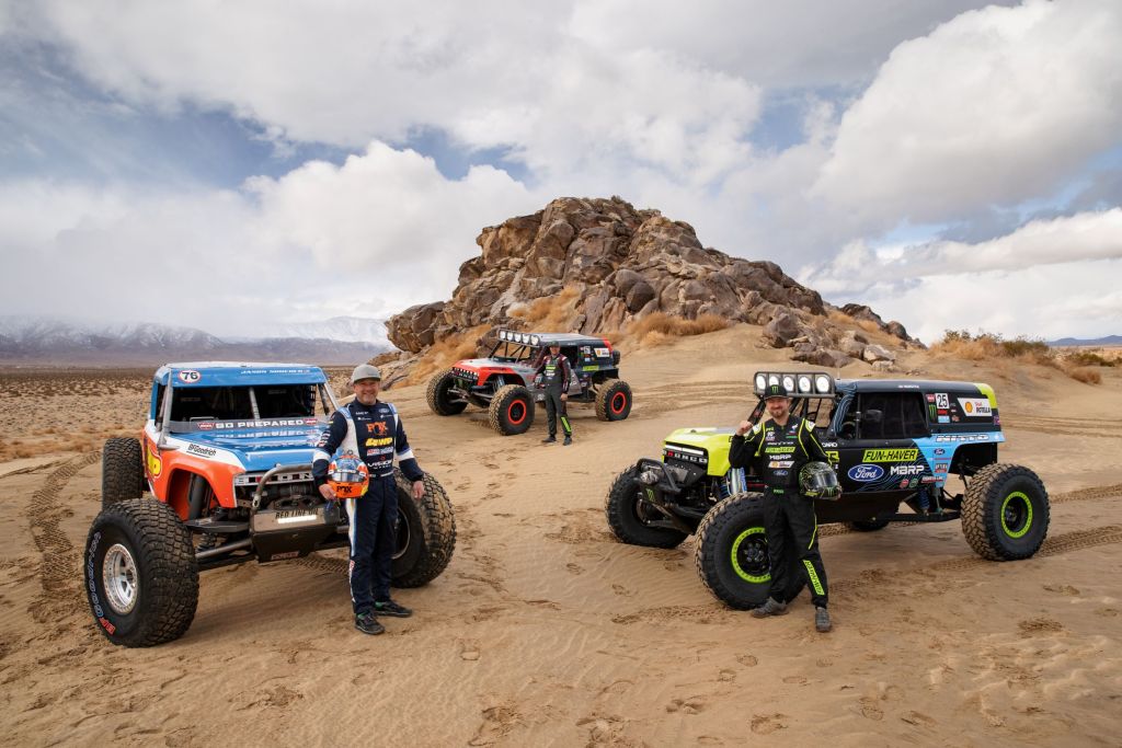 (Clockwise from left) Jason Scherer, Loren Hauley, and Vaughn Gittin, Jr., with their 2021 Ford Bronco 4400 King of the Hammers racers by a desert rock formation