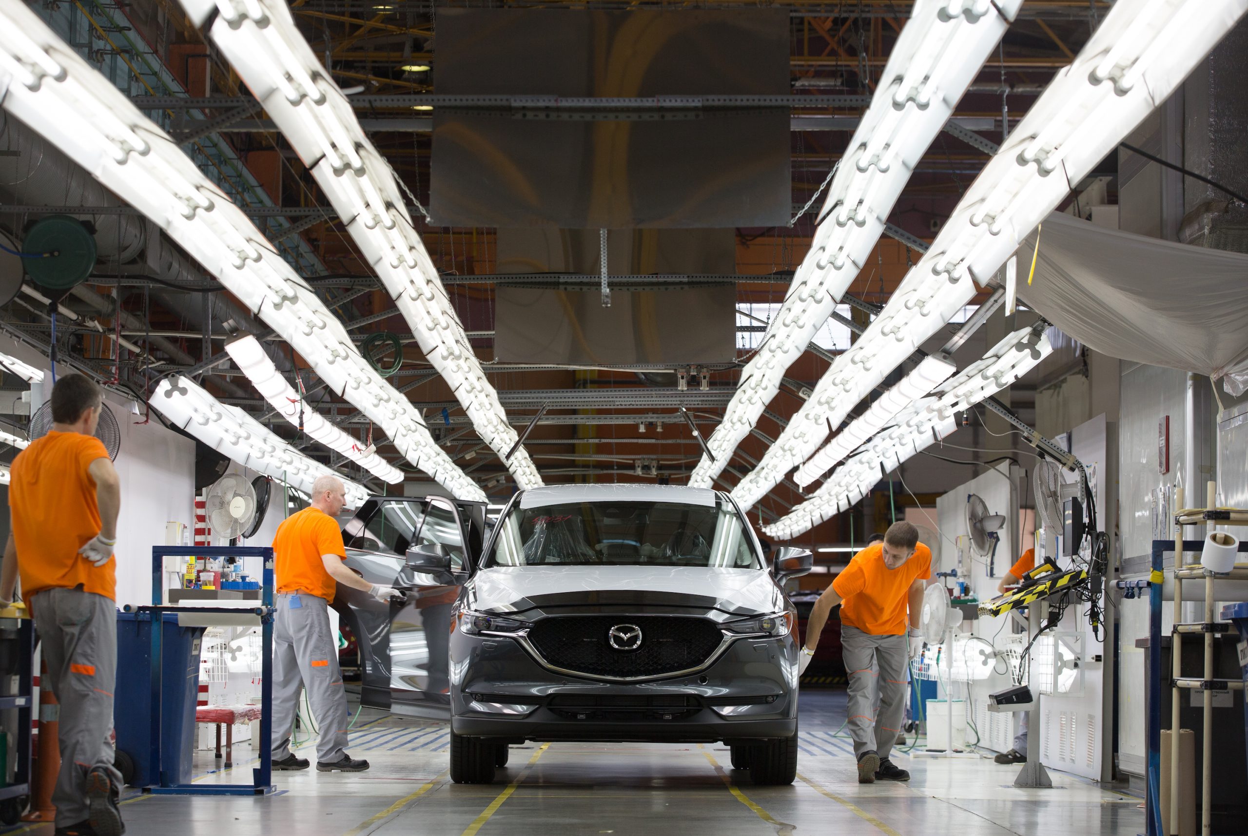 Workers check a Mazda Motor Corp. CX-5 sports utility vehicle (SUV) under inspection lights on the assembly line