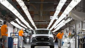 Workers check a Mazda Motor Corp. CX-5 sports utility vehicle (SUV) under inspection lights on the assembly line