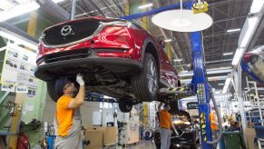 Workers affix parts to the underside of a Mazda Motor Corp. CX-5 sports utility vehicle (SUV) on the assembly line at the Mazda Sollers Manufacturing Rus LLC plant in Vladivostok, Russia, on Tuesday, Sept. 3, 2019