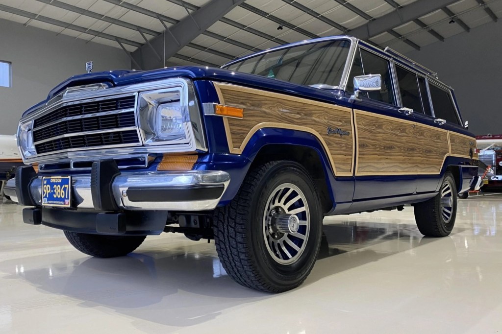 A low-angle front 3/4 view of a modified blue 1991 Jeep Grand Wagoneer in a hanger