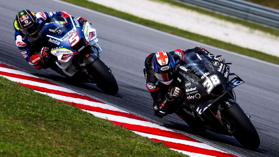 MotoGP riders Bradley Smith on a black-and-white bike and Johann Zarco on a white-and-blue bike countersteer their motorcycles around a corner