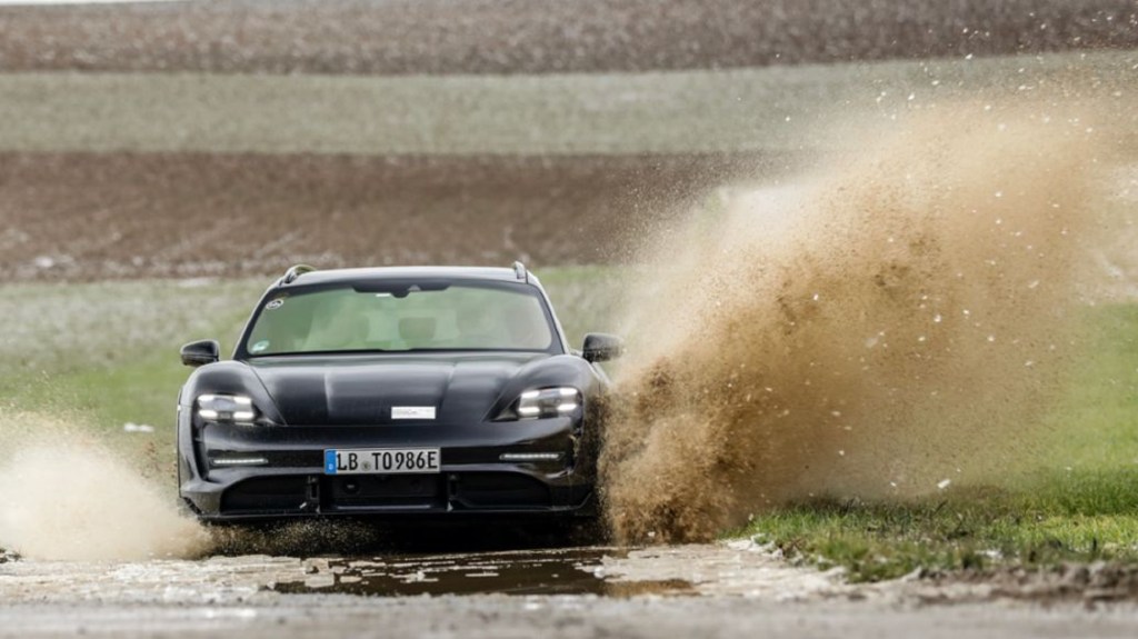 The front view of the black Porsche Taycan Cross Turismo prototype driving through a muddy and watery field