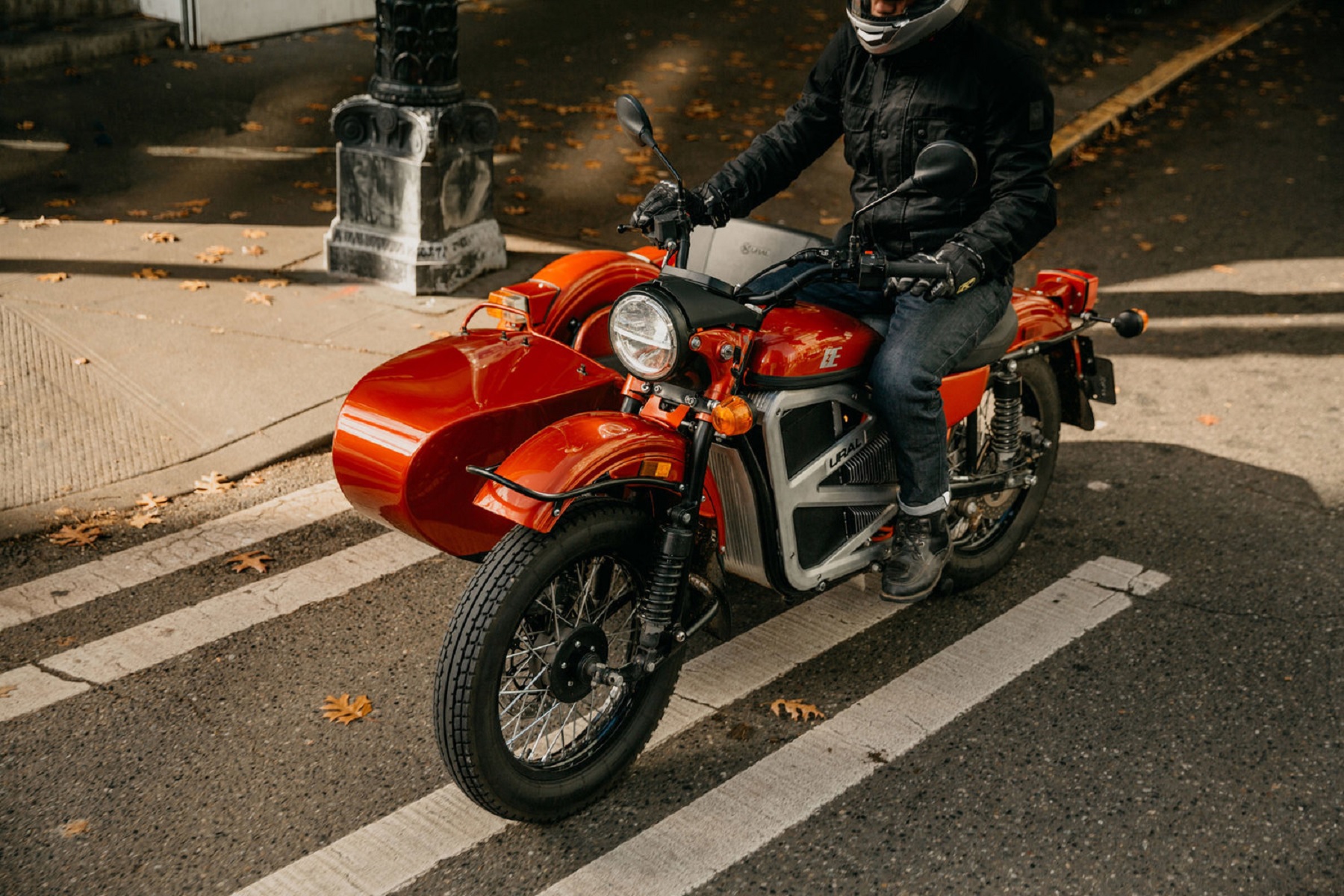 A rider on the orange Ural electric cT motorcycle concept with its sidecar on a city street