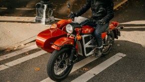 A rider on the orange Ural electric cT motorcycle concept with its sidecar on a city street